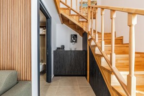 Ein modernes Interieur mit einer Holztreppe, einem dunklen Schrank und Blick auf eine Küstenlandschaft durch ein Fenster.
