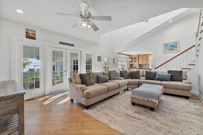 A spacious living room with a large sectional sofa, a ceiling fan, and a view of the outdoors through large windows.