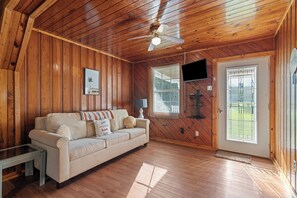 A cozy room with a wooden ceiling, a sofa, a television, and a window with blinds.