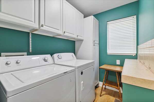 A laundry room with a washer and dryer, wooden stool, and teal walls.