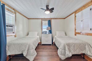 A room with two beds, a ceiling fan, a dresser, and a window with blinds.