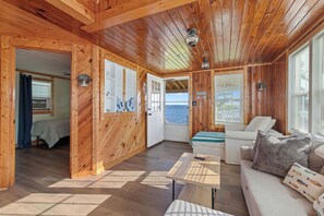 A wooden cabin interior with a bed, sofa, and a view of the sea through a door.