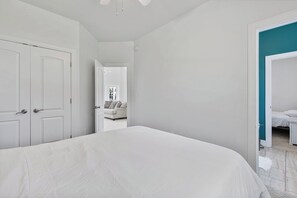 A bedroom with a large bed, a door leading to a bathroom, and a view into another room with a sofa.