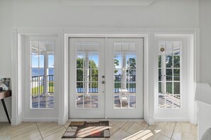 Ein Zimmer mit einer großen weißen Tür, einem kleinen Teppich und Blick auf eine Terrasse und Außenbereich.