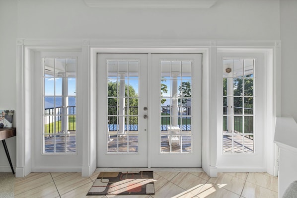 A room with a large white door, a small rug, and a view of a deck and outdoor area.