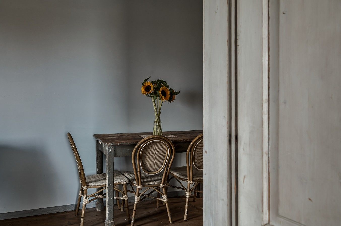 Ein rustikaler Esstisch mit einer Sonnenblumenvase, zwei Korbstühlen und einem Holzboden.