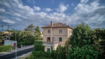 A two-story building with a red-tiled roof, surrounded by greenery and a clear sky.