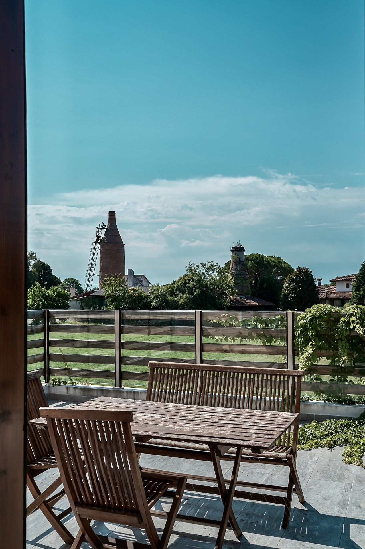 An outdoor patio with wooden furniture and a view of a windmill and fields.