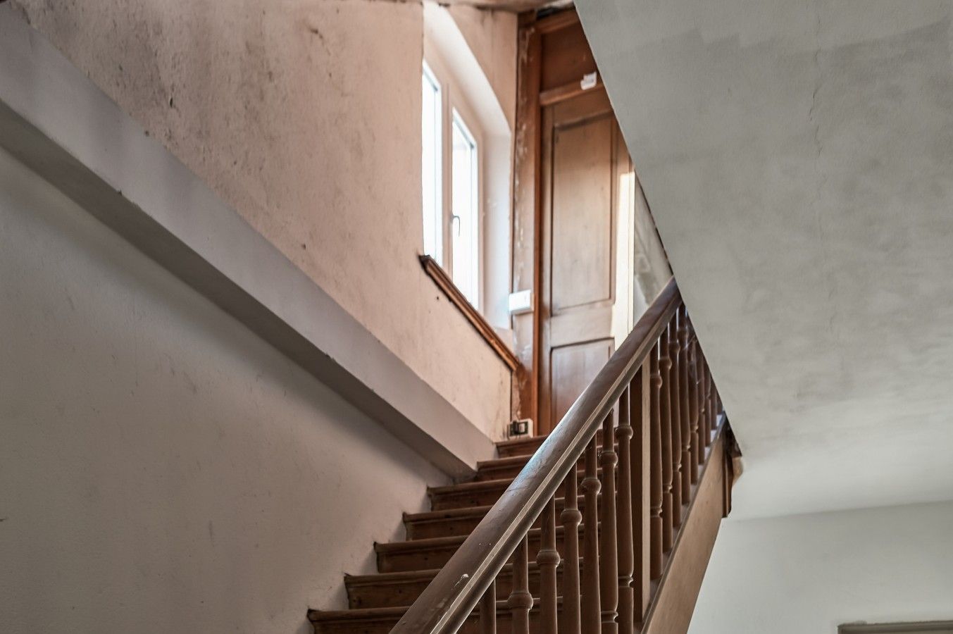 Eine Treppe mit Holzstufen und einem Metallgeländer, die zu einem Raum mit Fenster und Tür führt.