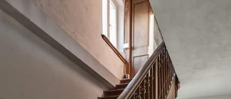 A staircase with wooden steps and a metal handrail, leading to a room with a window and a door.