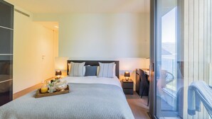 Ein modernes Hotelzimmer mit einem großen Bett, Nachttischen mit Lampen, einem Schreibtisch und einem Balkon mit einem Stuhl.