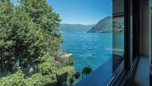 Blick aus einem Fenster auf einen See mit Bäumen und Hügeln im Hintergrund.