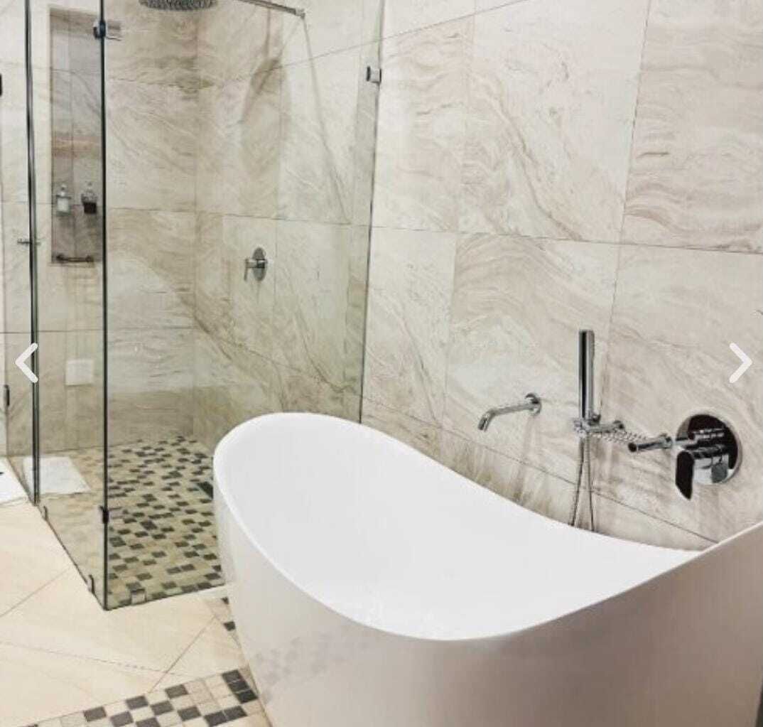 Un baño moderno con una bañera independiente, cabina de ducha de cristal y paredes de mármol.