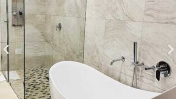 Un baño moderno con una bañera independiente, cabina de ducha de cristal y paredes de mármol.