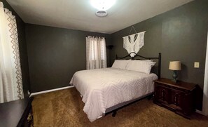 Un dormitorio con una cama, una mesita de noche, una lámpara y un adorno de macramé en la pared.