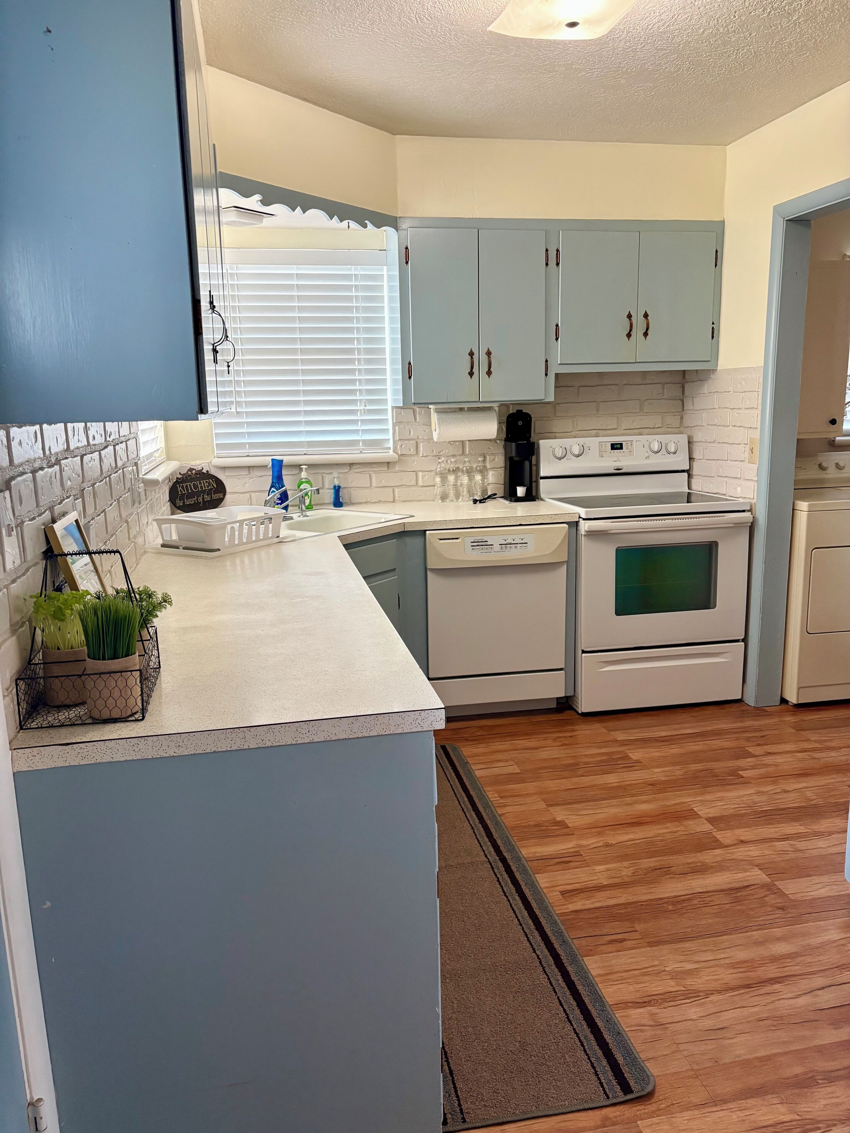 Una cocina con electrodomésticos blancos, gabinetes azul claro y una ventana con persianas.