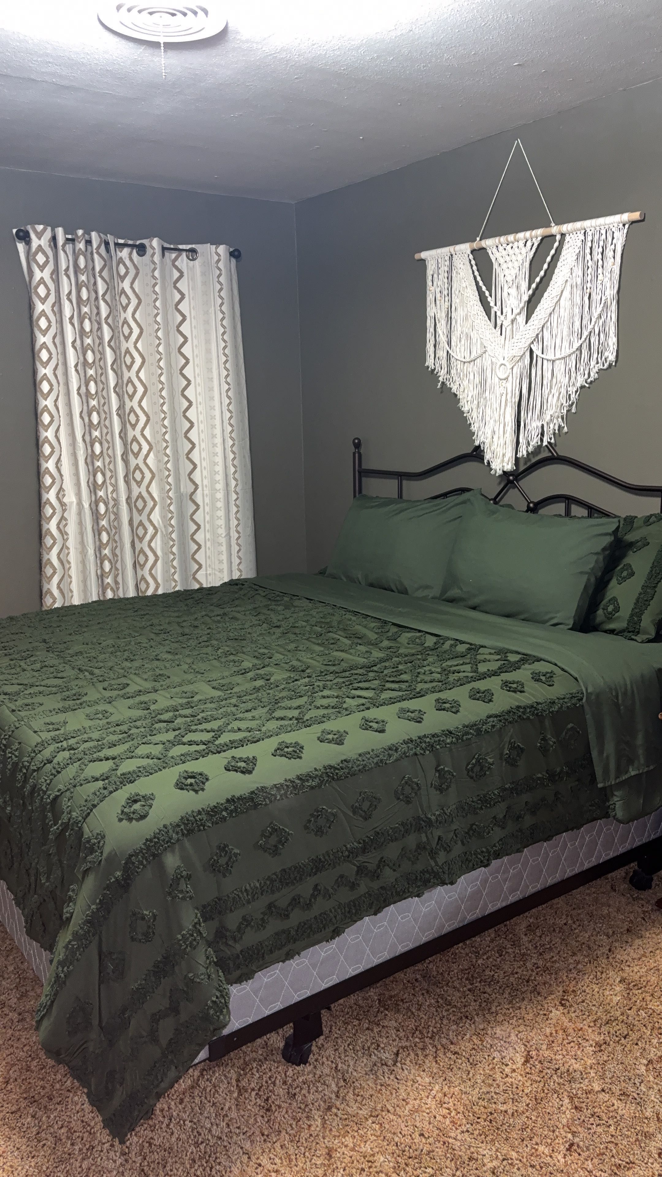 Un dormitorio con cama, un colgador de macramé y una cortina estampada.
