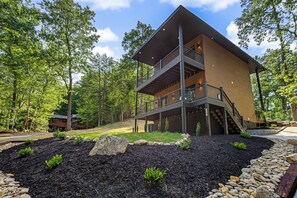 A two-story building with a balcony, surrounded by trees and a landscaped area with rocks and mulch. - Experience the perfect Pigeon Forge getaway at The Suite Life, a thoughtfully de (Pigeon forge)