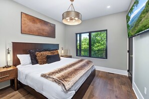 A bedroom with a large bed, a mounted TV, a window with a view of greenery, and a ceiling light fixture. - Experience the perfect Pigeon Forge getaway at The Suite Life, a thoughtfully de (Pigeon forge)