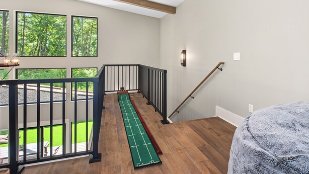 Een kamer met een houten vloer, een groen spelbord, een zwarte balustrade en uitzicht op een groen gazon door grote ramen.