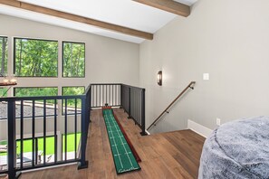 Une pièce dotée d’un plancher en bois, d’un jeu de soci été vert, d’une rambarde noire et offrant une vue sur une pelouse verdoyante grâce à de grandes fenêtres.