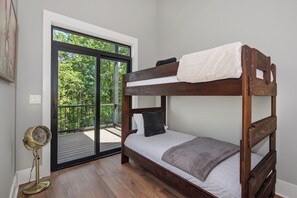A bunk bed with a white mattress and a gray blanket, a standing fan, and a sliding glass door leading to an outdoor deck. - Experience the perfect Pigeon Forge getaway at The Suite Life, a thoughtfully de (Pigeon forge)