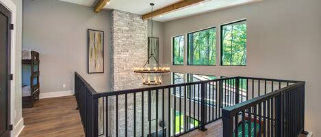 A spacious interior with a stone fireplace, large windows, and a wooden staircase.