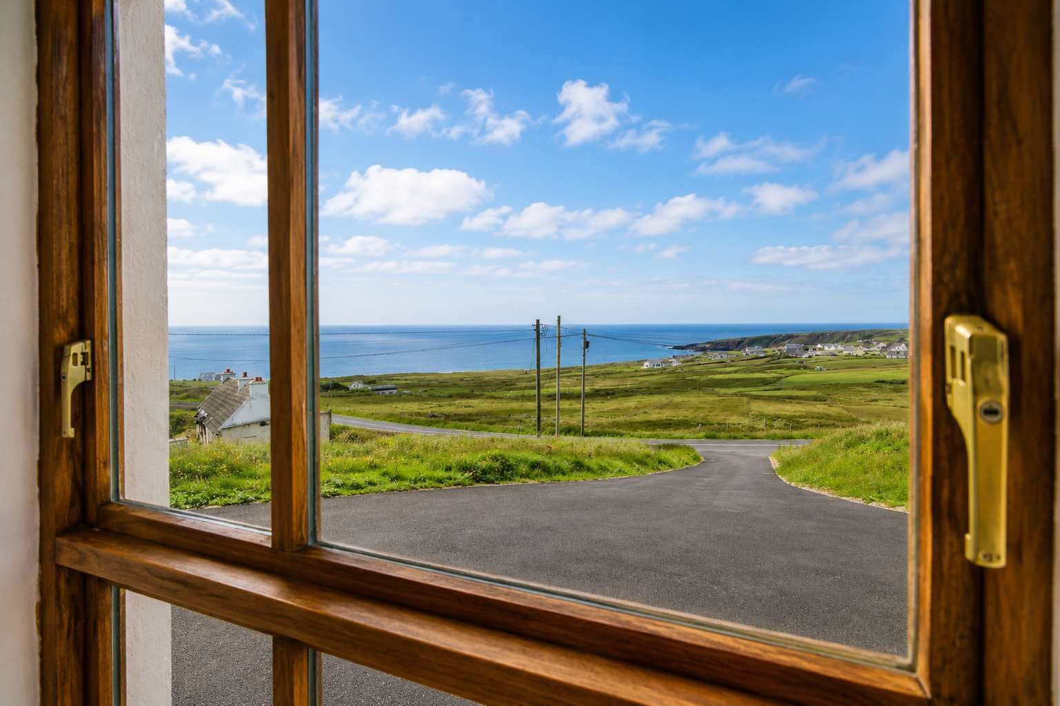 A view through a window of a rural road leading to the sea, with houses and grassy fields.