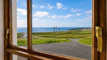 A view through a window of a rural road leading to the sea, with houses and grassy fields.