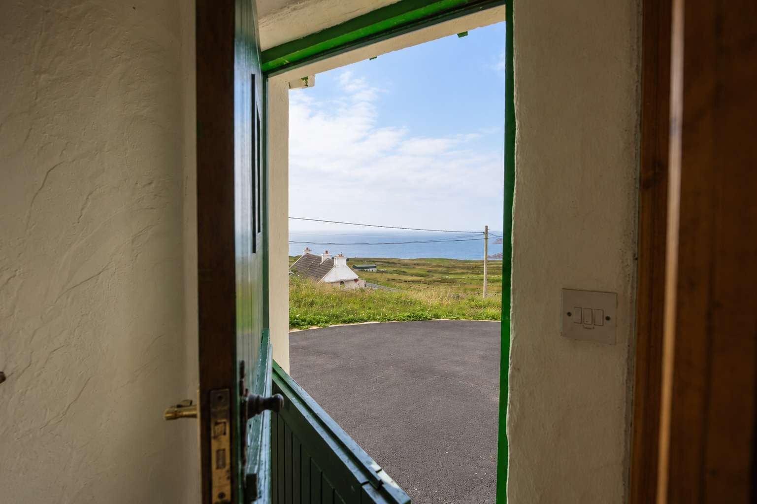 A doorway leading to a paved area with a grassy landscape and houses in the distance.