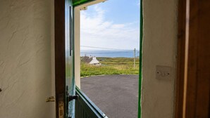 A doorway leading to a paved area with a grassy landscape and houses in the distance. - 4 Bedroom Irish Traditional Cottage with Sea View (Gweedore)