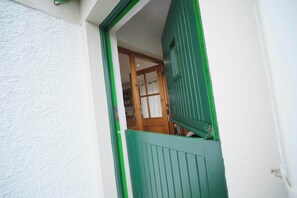 A view through a green-framed window with a white wall, revealing a room with a wooden door and a white curtain.