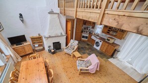 A wooden-floored living area with a dining table, chairs, a sofa, a fireplace, a kitchen with wooden cabinets, and a laundry area. - 4 Bedroom Irish Traditional Cottage with Sea View (Gweedore)
