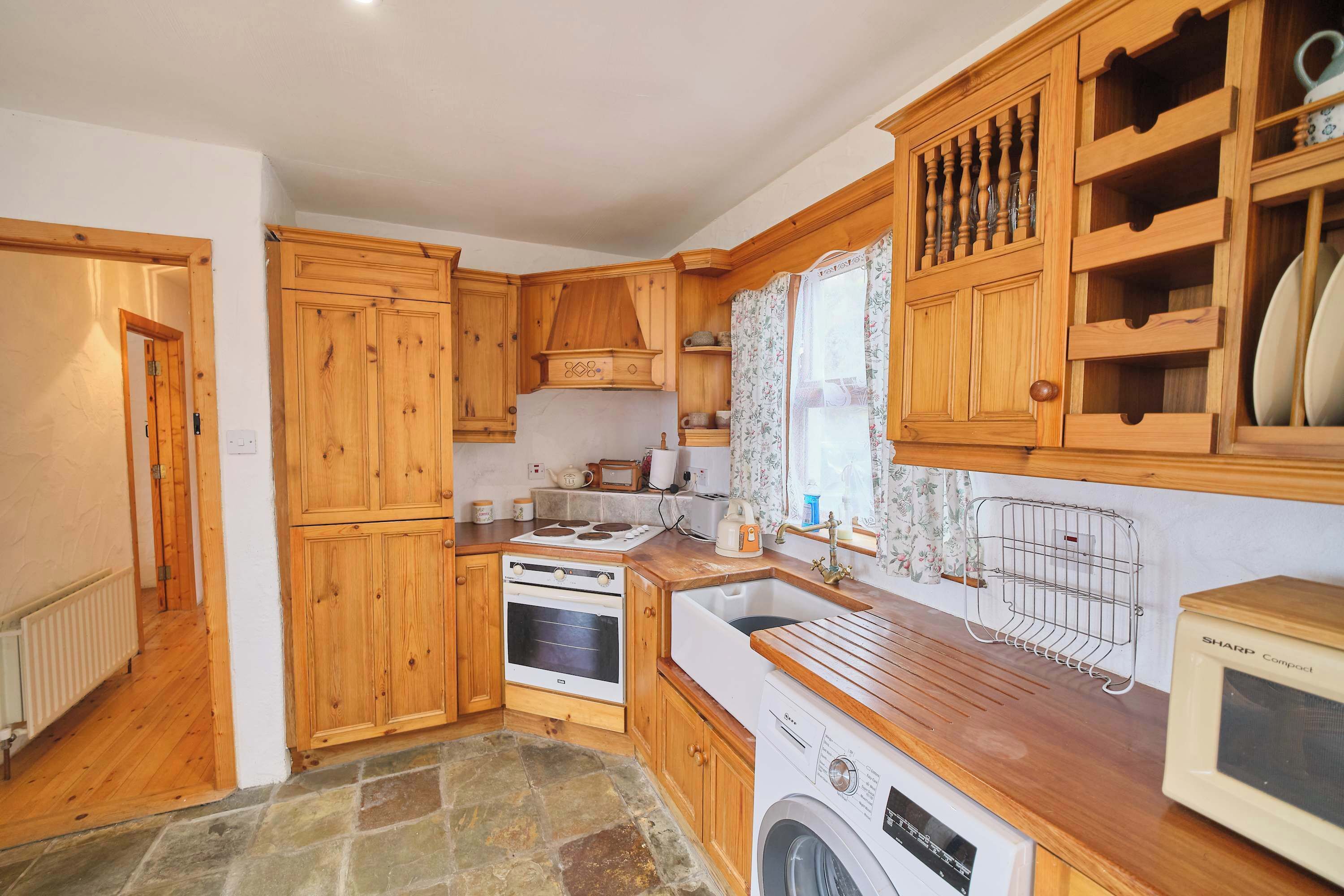 A compact kitchen with wooden cabinets, a washing machine, a microwave, and a sink.