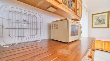 Un four à micro-ondes compact posé sur un plan de travail en bois, une grille métallique avec un témoin lumineux rouge et un tableau encadré accroché au mur.