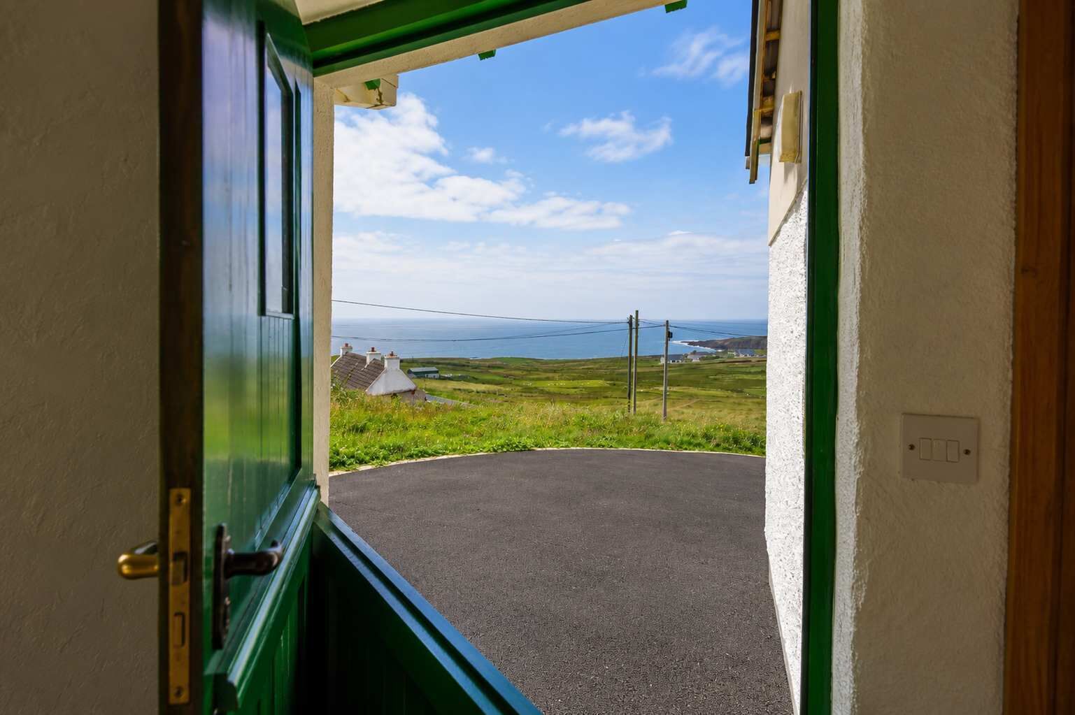 A doorway leading to a curved driveway with a view of the sea and houses in the distance.
