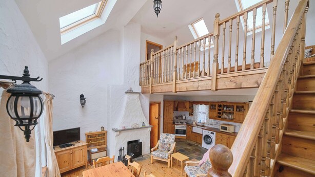 A spacious loft with a wooden staircase, a dining area, a kitchen, and a fireplace. - 4 Bedroom Irish Traditional Cottage with Sea View (Gweedore)