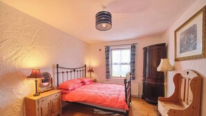 A bedroom with a bed, bedside lamps, a wooden dresser, a window with curtains, a radiator, and a framed picture on the wall. - 4 Bedroom Irish Traditional Cottage with Sea View (Gweedore)