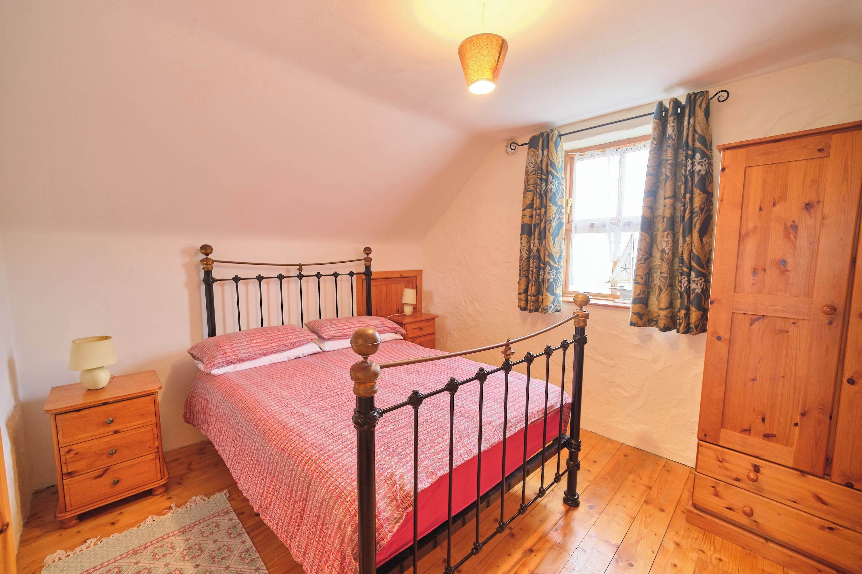 A bedroom with a bed, wooden wardrobe, and a window with curtains.
