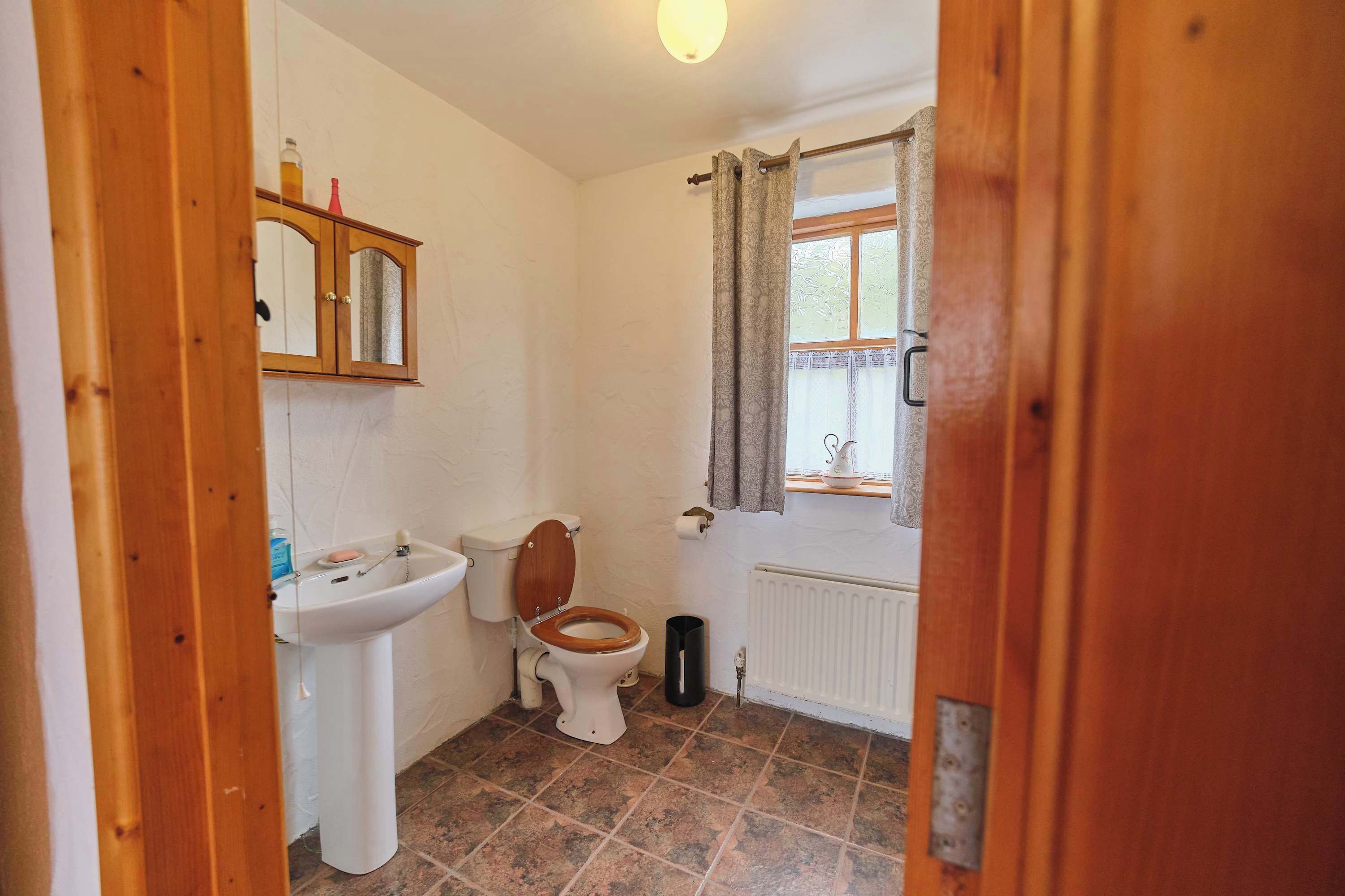 A bathroom with a toilet, sink, and window with curtains.