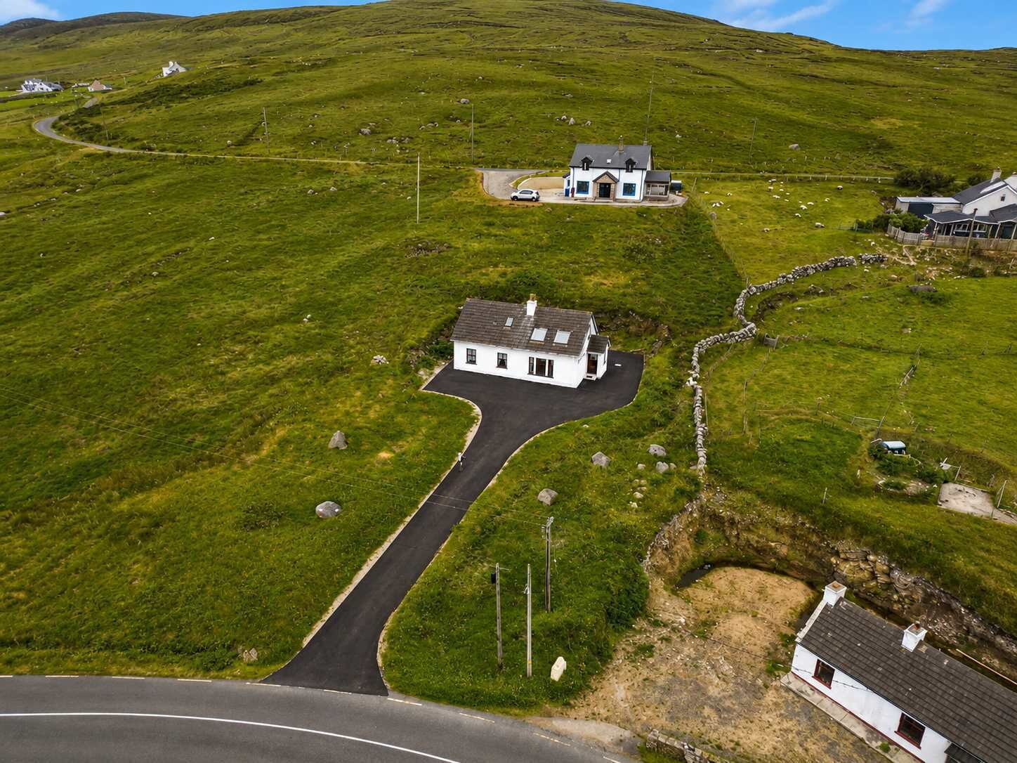 A rural landscape with a white house, a winding driveway, and a stone wall.