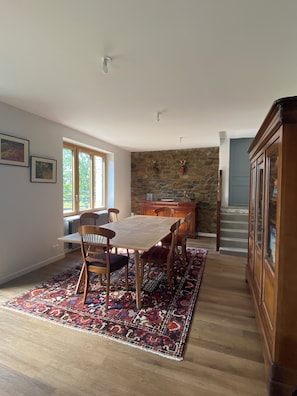 Zona pranzo con tavolo e sedie in legno, tappeto decorato e parete in pietra.