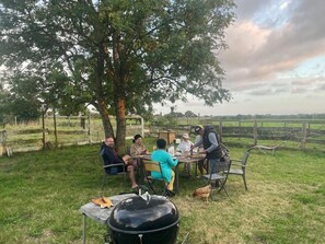 A group of people dining outdoors at a table with a tree and a rural landscape in the background. - Charming Family House 10 min from Mont-Saint-Michel – Sleeps 10 (Servon)