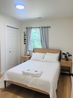 Una cama bien tendida con ropa blanca, cabecera de madera y dos mesitas de noche con lámparas.