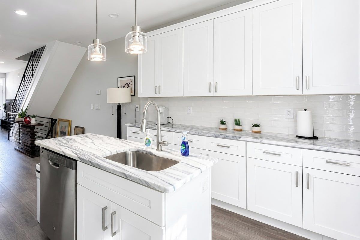 A modern kitchen with white cabinetry, a marble countertop, and pendant lighting.