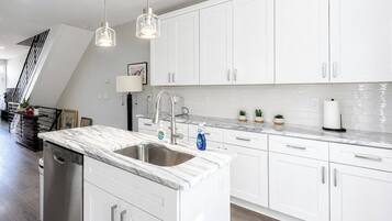 A modern kitchen with white cabinetry, a marble countertop, and pendant lighting.