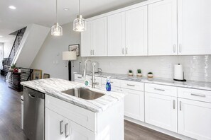 Een moderne keuken met witte kasten, een marmeren aanrechtblad en hanglampen.