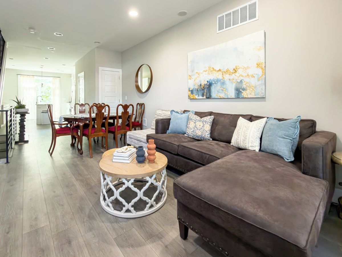 A living room with a brown sofa, a round coffee table, and a dining area with wooden chairs and a table.
