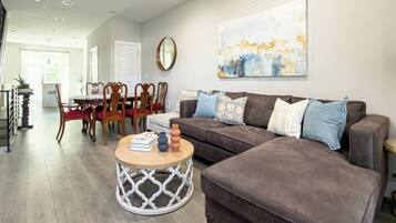 A living room with a brown sofa, a round coffee table, and a dining area with wooden chairs and a table.