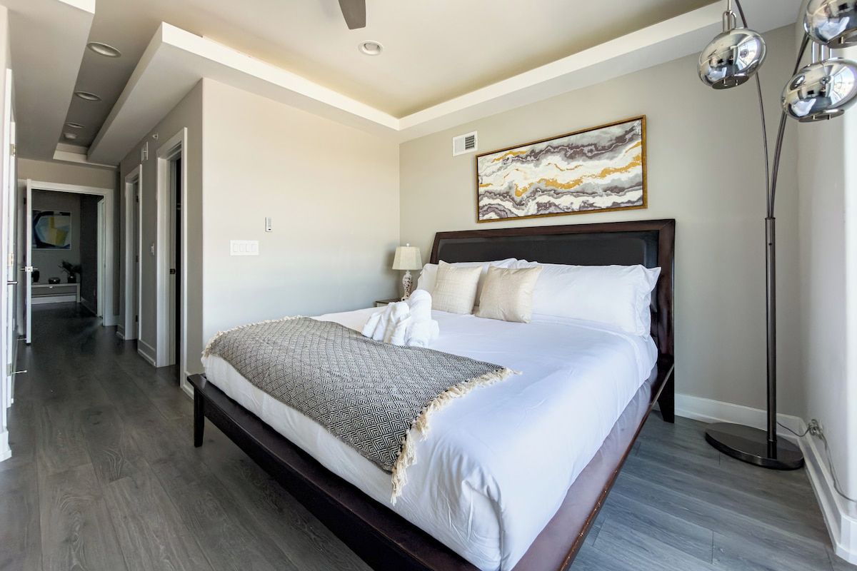 A hotel room with a large bed, a floor lamp, and a painting on the wall.